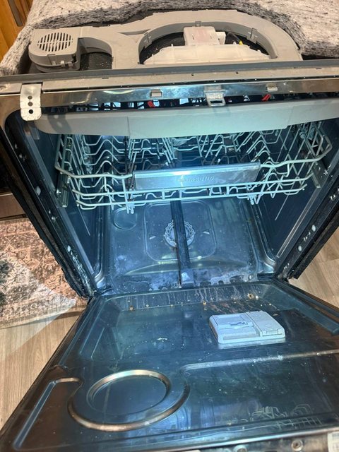 Samsung dishwasher with the door open, racks in place and the drain assembly and filter set on the counter