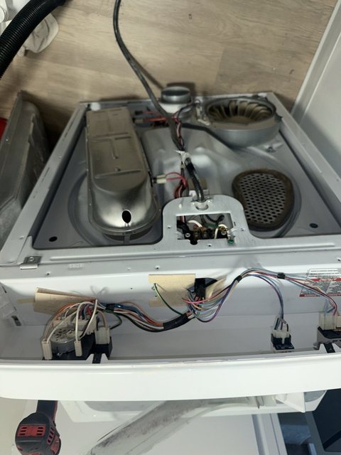 Electric dryer with the top raised, heating element and blower wheel exposed, drill on the floor